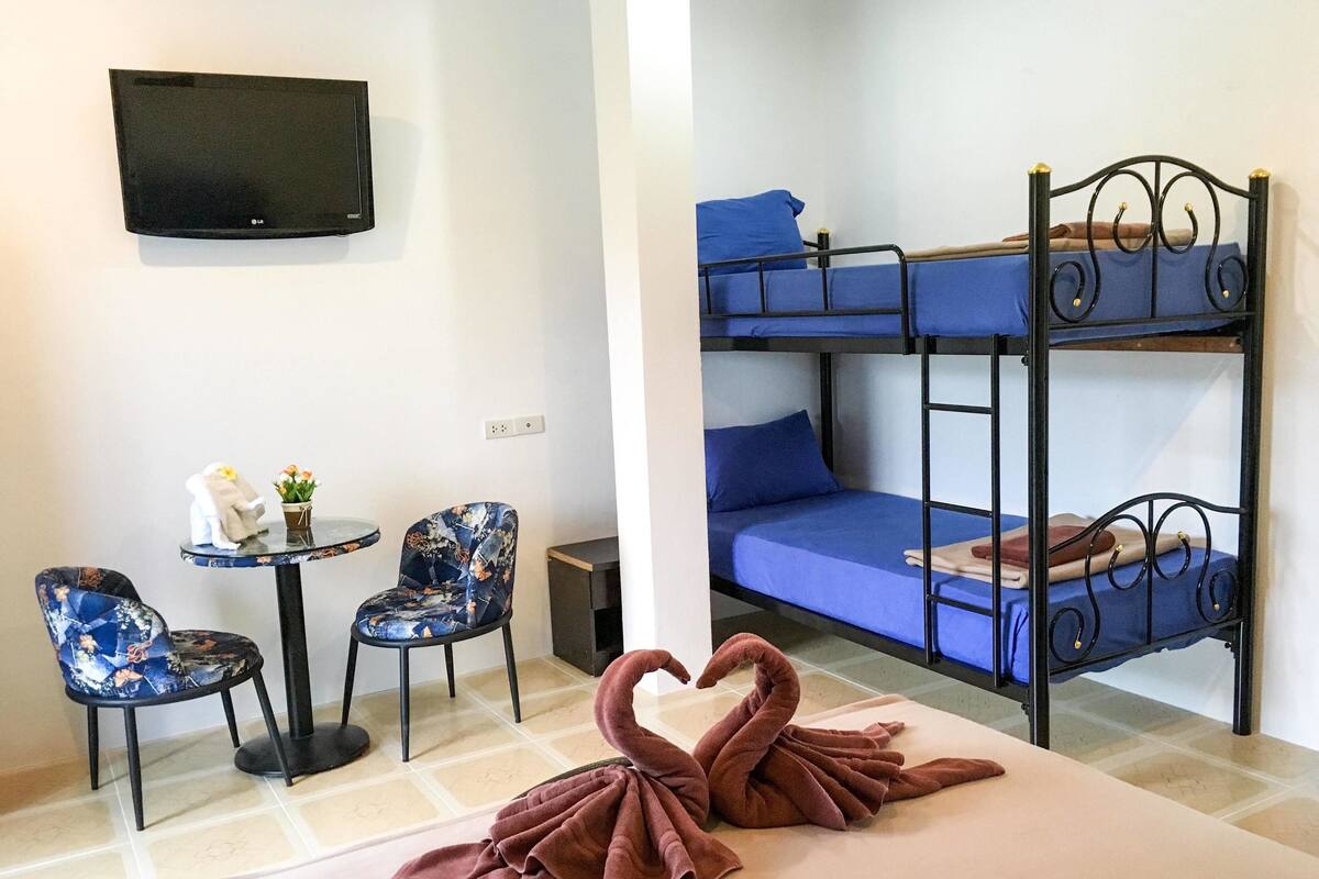 A room with bunk beds, a small table with chairs, a TV mounted on the wall, and a swan-shaped towel on the floor.