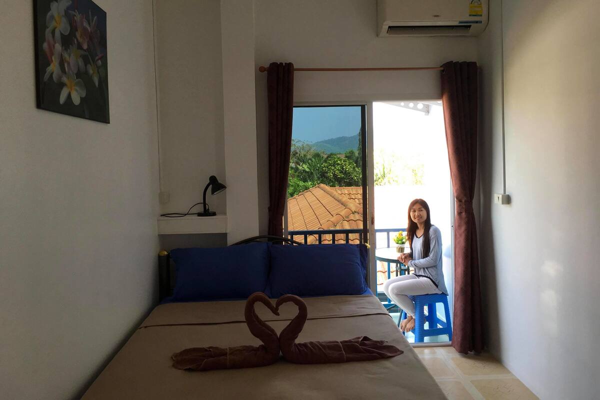 A bedroom with a bed, a desk, a chair, and a view of the outdoors.