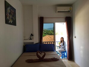 Quarto com cama, escrivaninha, cadeira e vista para o exterior.