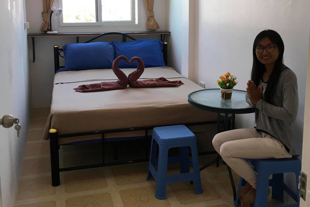 A small, neatly arranged room with a bed, a table, and a stool.
