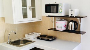Una cocina compacta equipada con lavamanos, microondas, cocedor de arroz, hervidor de agua y tostadora.