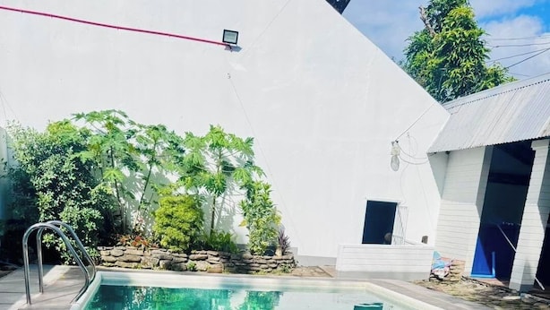 A rectangular swimming pool with clear blue water, surrounded by a white wall and a stone border. - Country Inn  Baggao- Annex (Baggao)