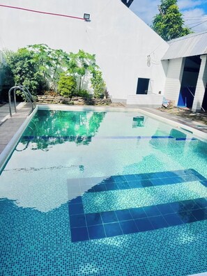 A rectangular swimming pool with clear blue water, surrounded by a white wall and a stone border. - Country Inn Baggao- Annex (Baggao)