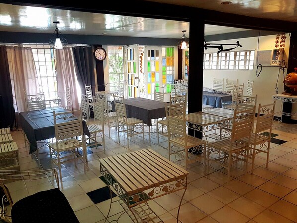A dining area with white metal chairs and tables, a clock on the wall, and colorful window panes. - Country Inn Baggao- Annex (Baggao)