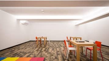 A spacious room with a high ceiling, wooden flooring, and a colorful foam mat at the entrance.