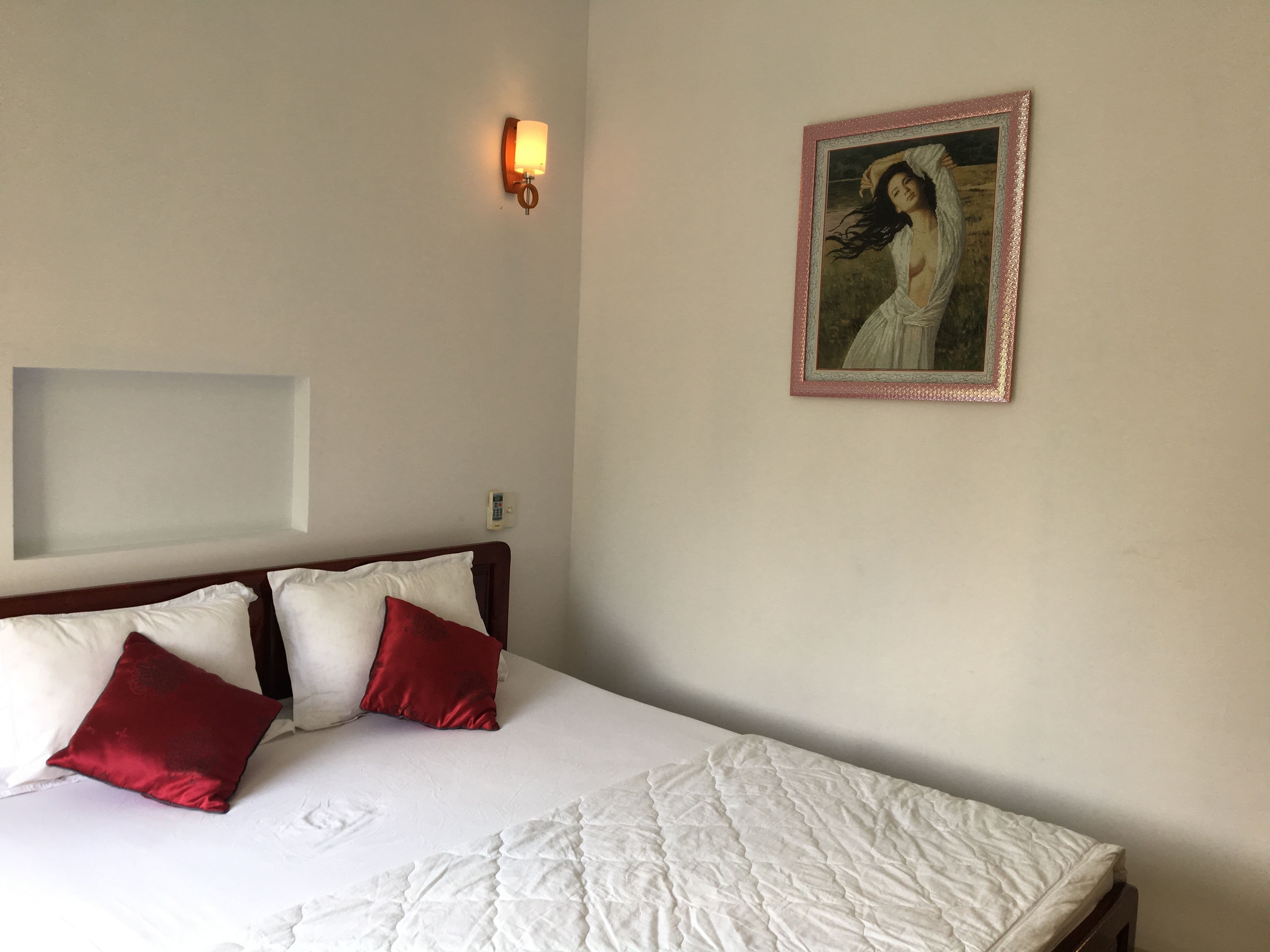 Una camera d'albergo con un letto, due cuscini, una lampada a muro e un quadro incorniciato.
