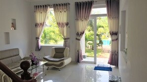 A spacious living room with a sofa, armchair, and a glass coffee table. There is a staircase with a wooden handrail leading to another level. - Areca Resort Cay Cau (Mui Ne)