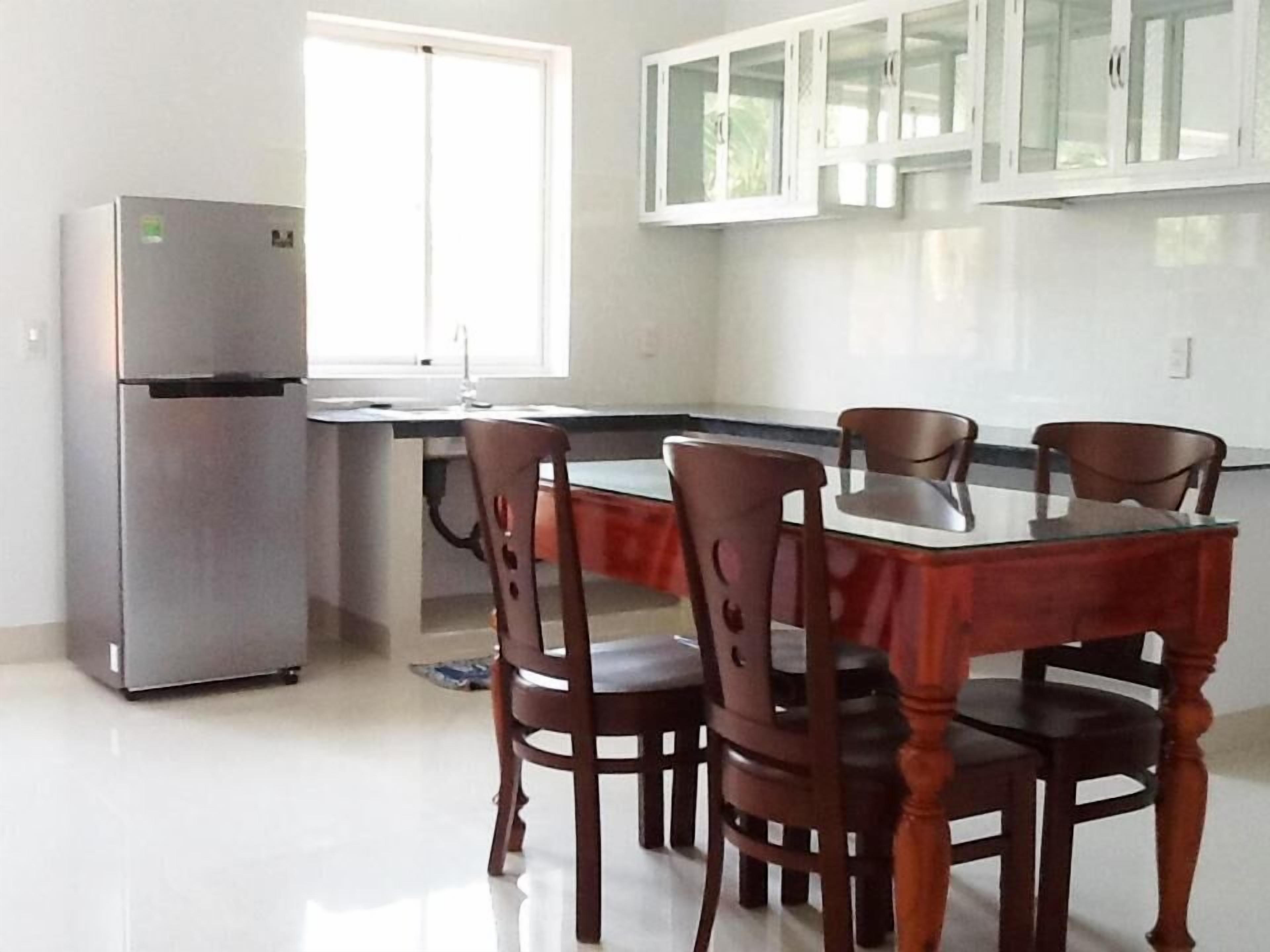 A kitchen with a refrigerator, a dining table with chairs, and white cabinets above the counter.