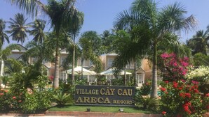 A sign for Village Cau Areca Resort surrounded by lush greenery and palm trees. - Areca Resort Cay Cau (Mui Ne)