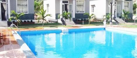 A swimming pool with a tiled deck, surrounded by small white buildings with steps leading up to the entrance.