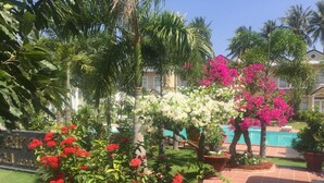 A landscaped garden with a pool, palm trees, and flowering plants. - Areca Resort Cay Cau (Mui Ne)