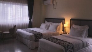 Ein Hotelzimmer mit zwei Betten, einem Sessel, einer Klimaanlage und einer Lampe.