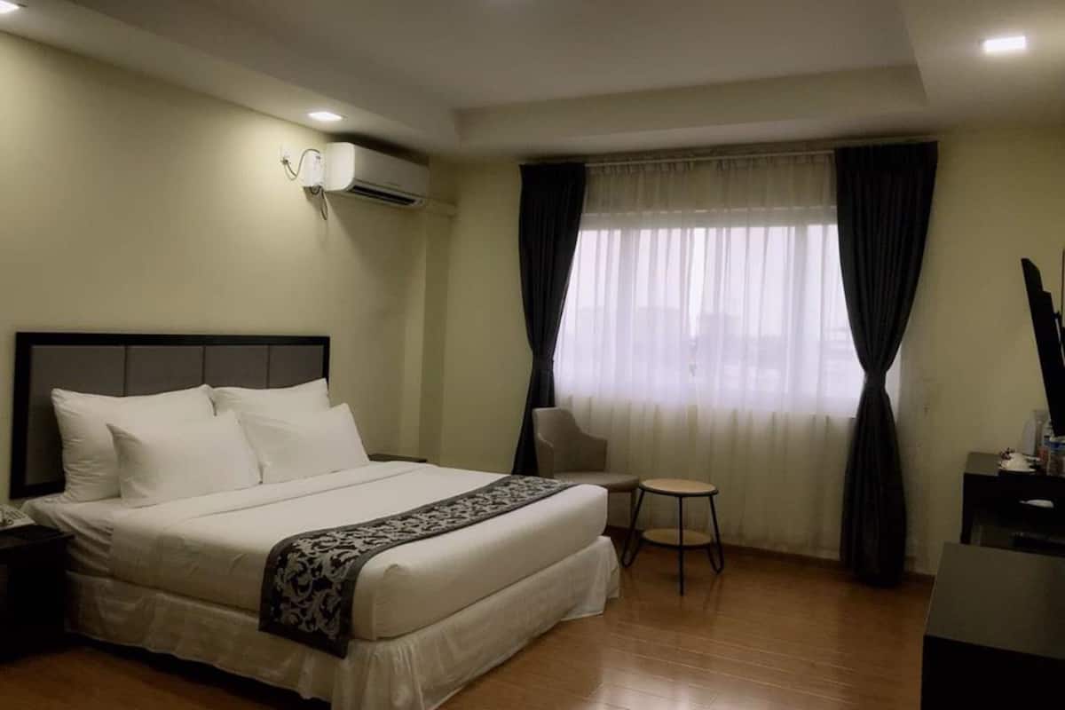 A hotel room with a bed, a chair, a desk, and a window with curtains.