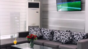 Ein modernes Wohnzimmer mit einem grauen Sofa, gemusterten Kissen, einem Glastisch und einem an der Wand befestigten Flachbildfernseher.