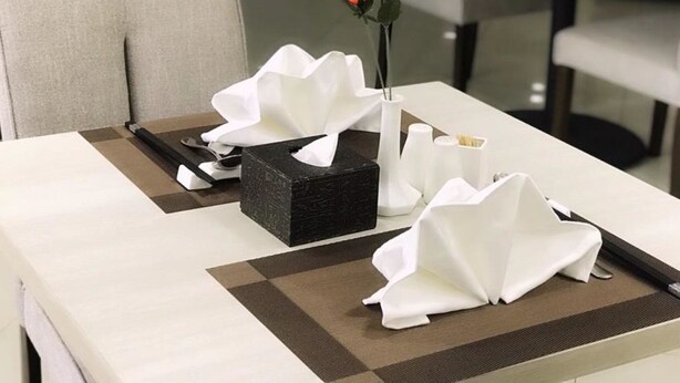 Ein Esstisch im Hotel, gedeckt mit einer schwarzen Schachtel, weißen Servietten und einer einzelnen orangefarbenen Rose in einer Vase.