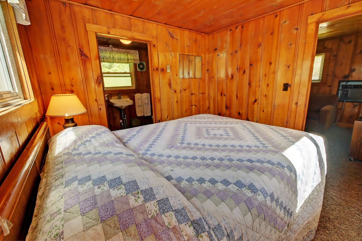 Une chambre à coucher aux murs lambrissés, avec un lit, une table de chevet et une fenêtre.