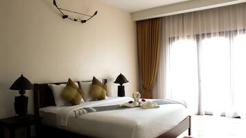 A hotel room with a large bed, two bedside lamps, a decorative wall piece, and a view of the outdoors through sheer curtains.