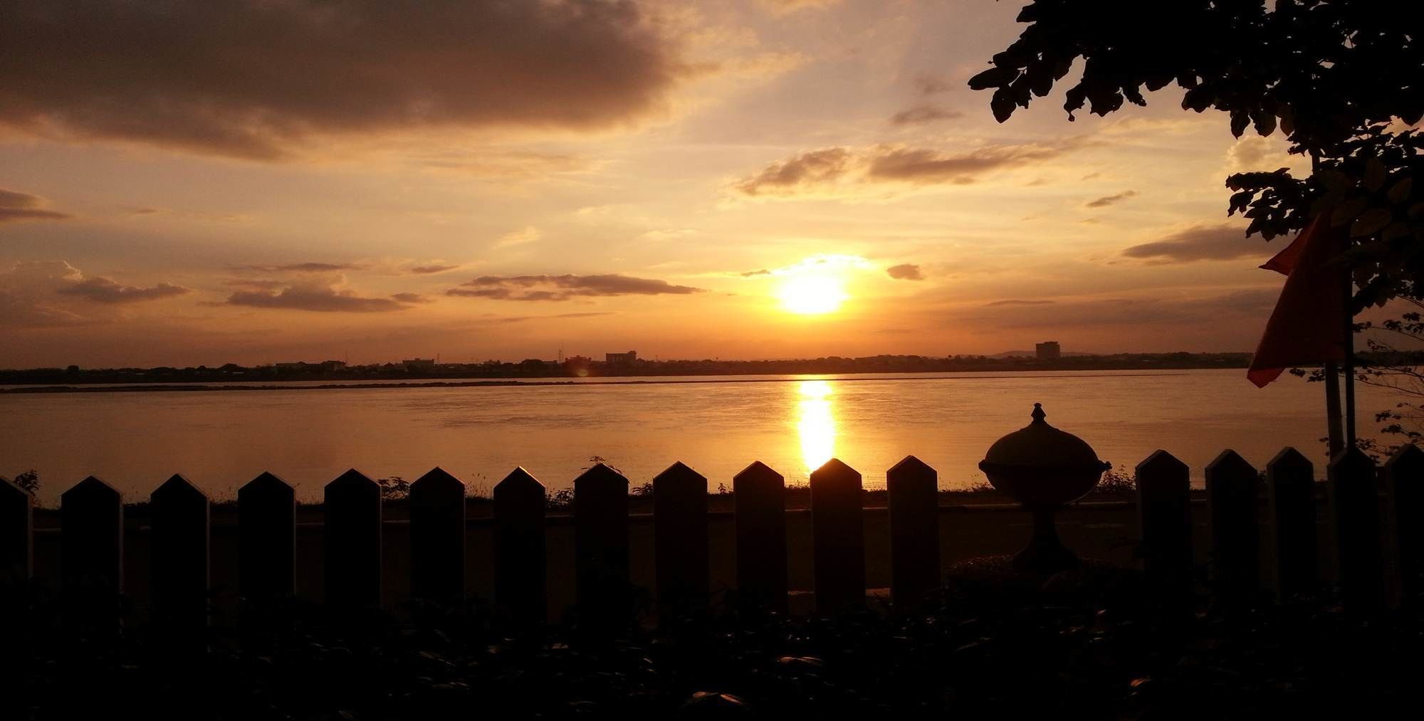 A sunset over a body of water with a fence in the foreground.