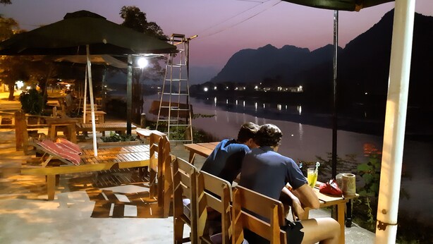 A riverside dining area with wooden furniture and a ladder. - Diep Le Homestay (Phong Nha)