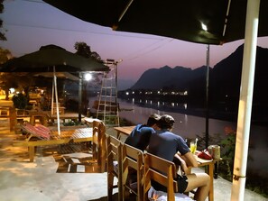 A riverside dining area with wooden furniture and a ladder. - Diep Le Homestay (Phong Nha)