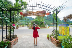 A woman in a red dress standing under a wooden archway with a sign that reads "Diep Le Homestay". - Diep Le Homestay (Phong Nha)