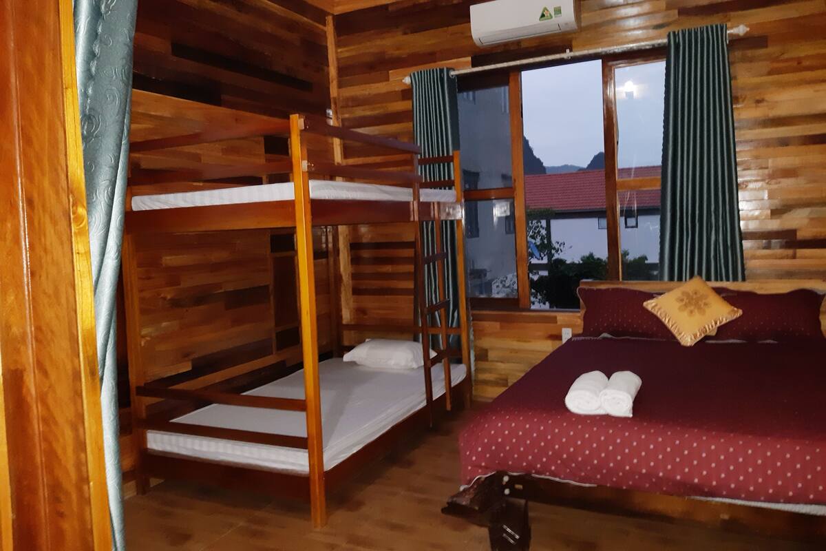 A wooden cabin room with bunk beds, a bed with a red polka dot cover, and a window with curtains.
