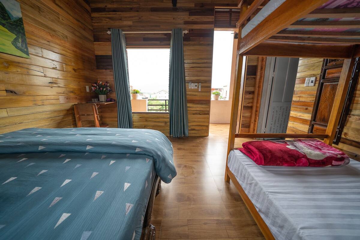 A wooden cabin-style room with two beds, a small table, and a window with curtains.