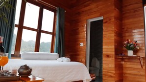 A wooden cabin room with a bed, a table with a teapot, a bottle, and a glass of orange juice. - Diep Le Homestay (Phong Nha)
