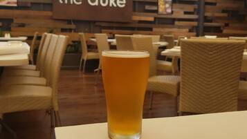 A glass of beer on a table in a restaurant with a sign reading "the duke" in the background.