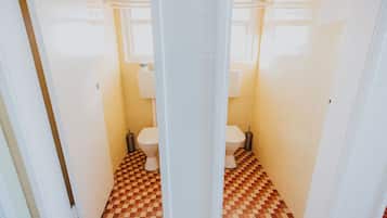 Un baño con baldosas de piso a cuadros, dos inodoros y paredes blancas.