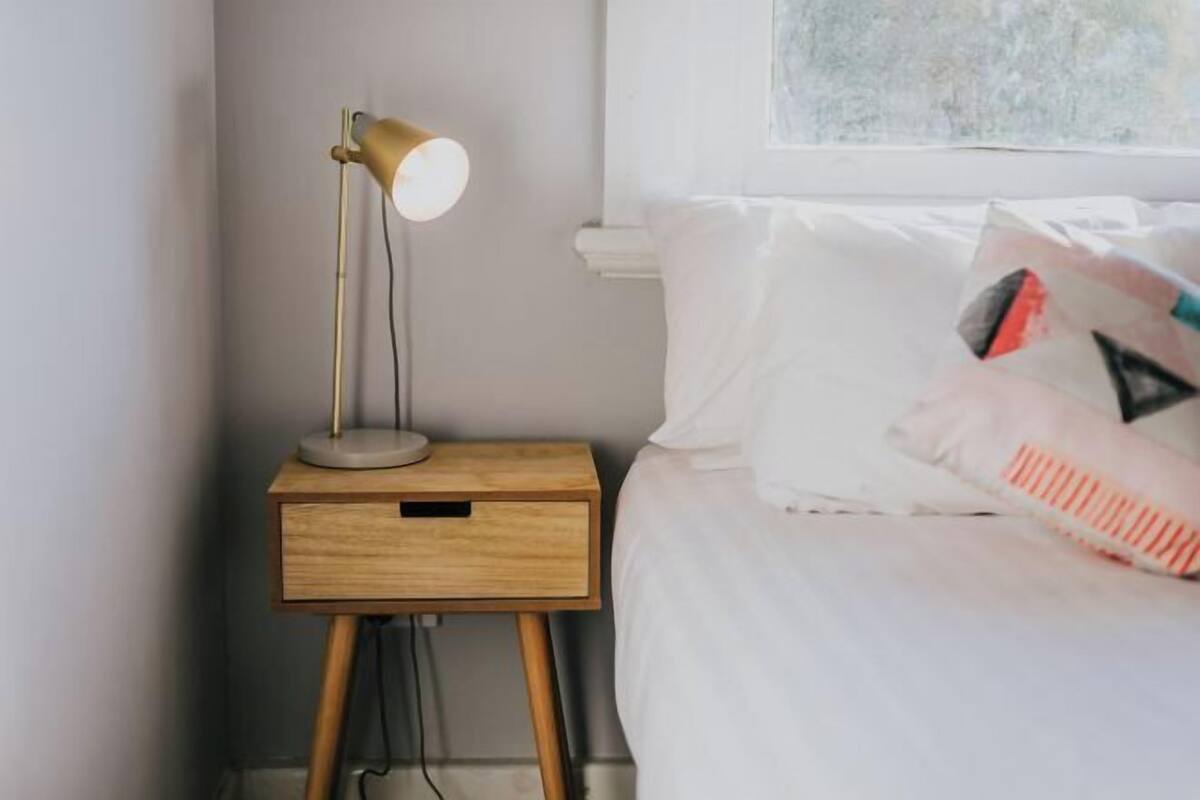 A neatly made bed with white bedding and a bedside lamp on a wooden nightstand.