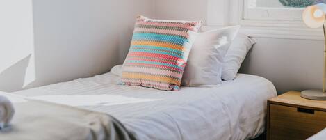 A neatly made bed with white bedding and a colorful striped pillow.