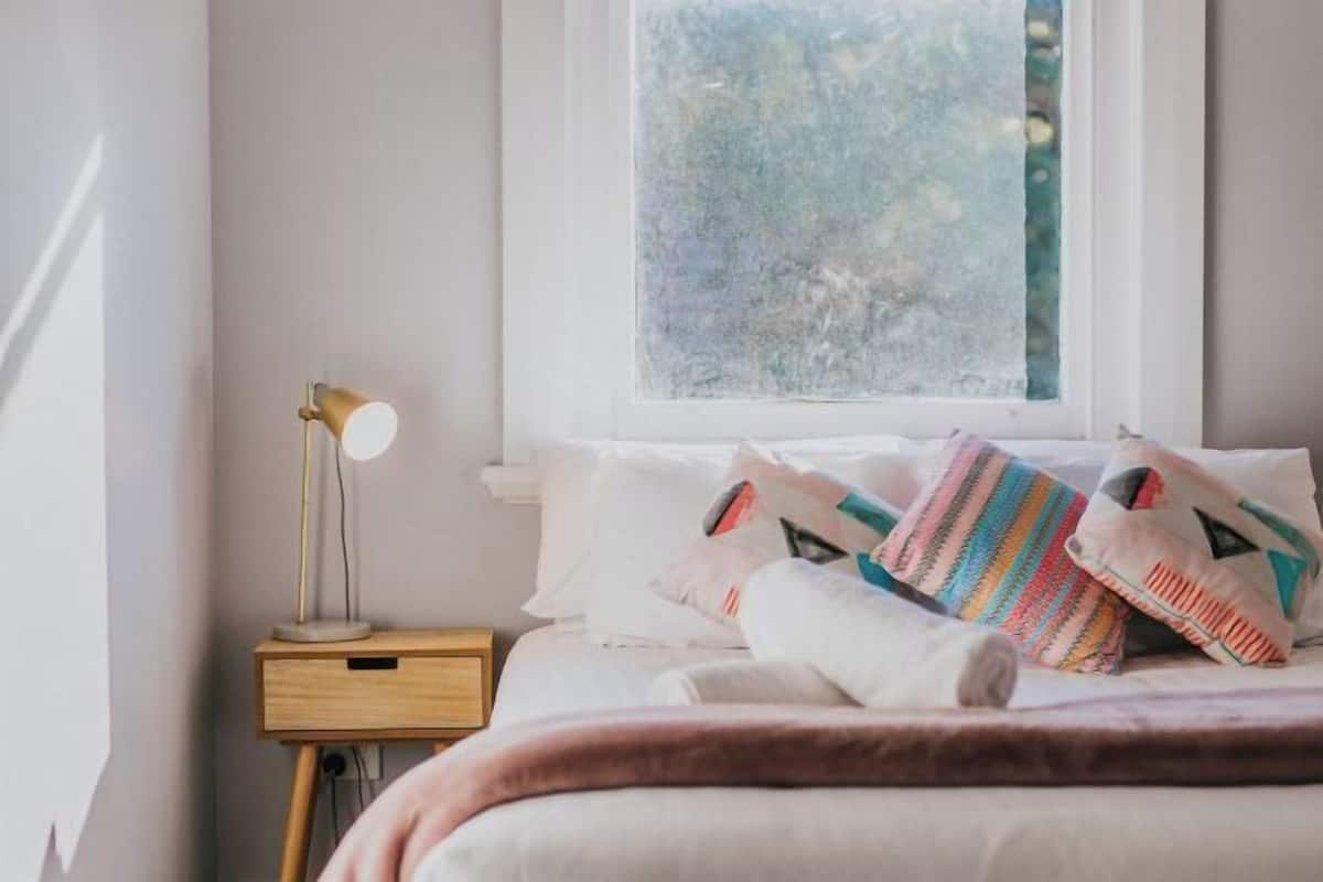 A bedroom with a bed, pillows, a bedside lamp, and a window with a view.