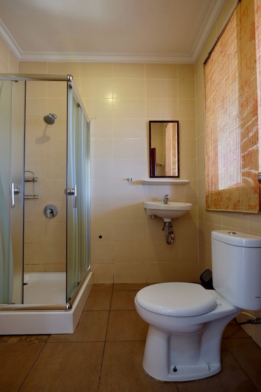 Un baño con ducha envuelta en vidrio, inodoro blanco y lavamanos con espejo sobre él.