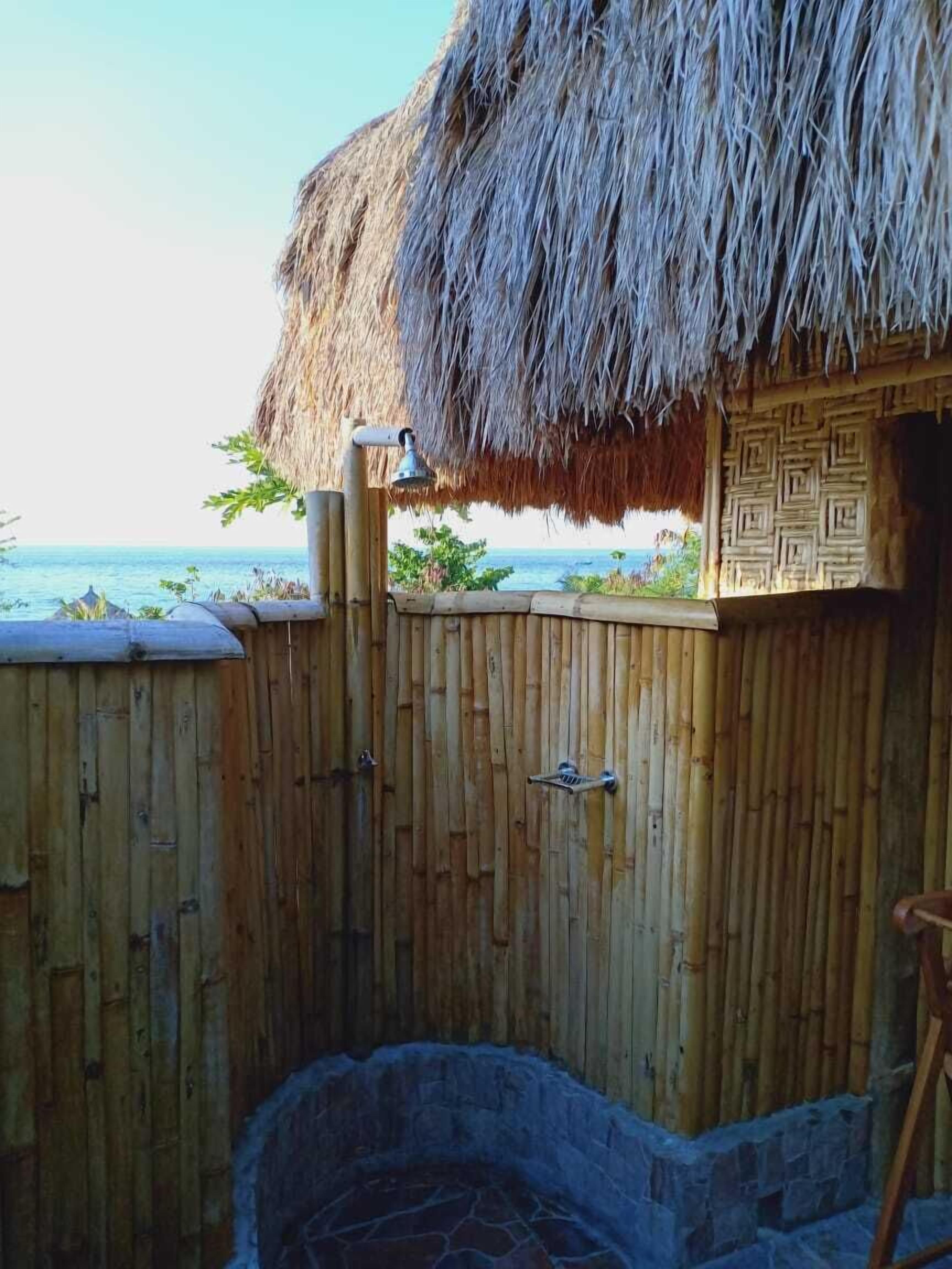 A thatched-roof structure with a bamboo fence and a stone-built hot tub area.