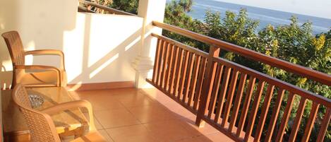 A balcony with a wooden railing, a glass table, and wicker chairs.