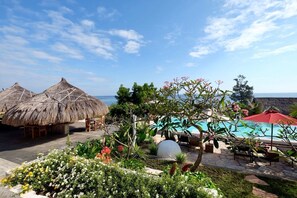 A poolside area with thatched umbrellas, lounge chairs, and a view of the sea.