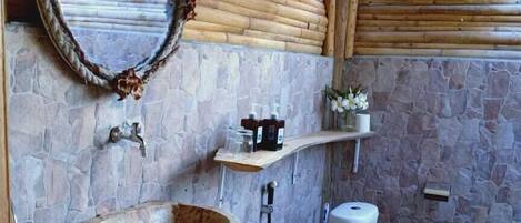 A bathroom with a stone wall, a wooden basin, a toilet, and a mirror.