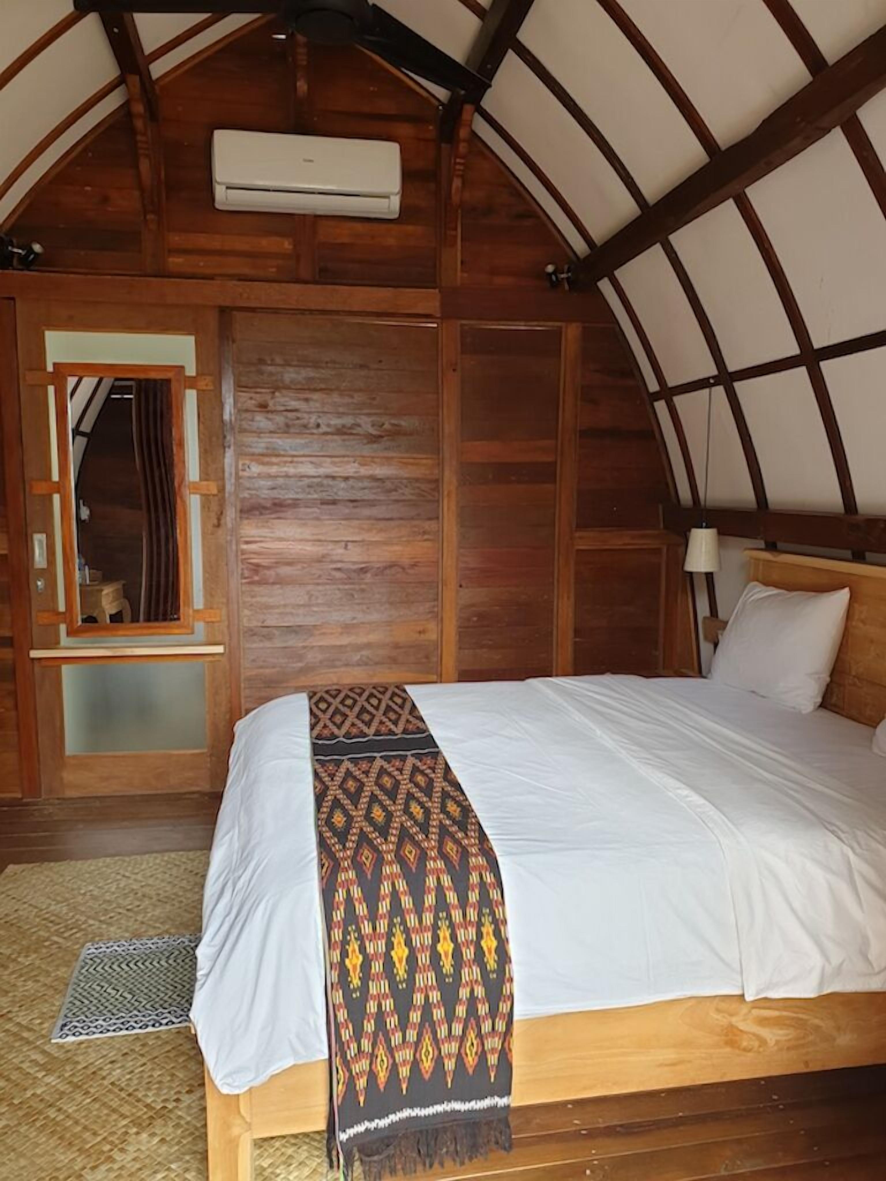 A wooden-framed bedroom with a bed, a nightstand, a mirror, and an air conditioning unit.