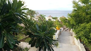 A pathway leading to a beach with lush greenery and a view of the ocean. - Mario Hotel and Cafe (Tambolaka)