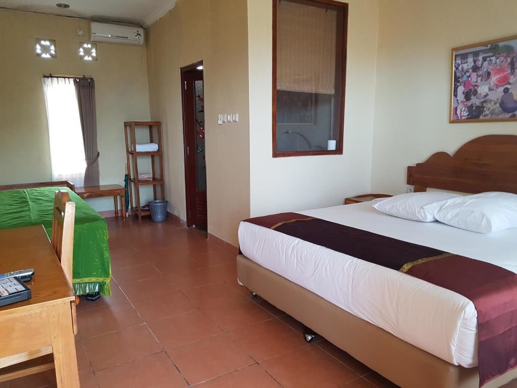 A hotel room with a single bed, a wooden headboard, a green sofa, a small table with a remote control, and a window with curtains.