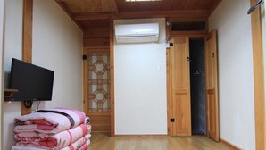 A hallway with wooden flooring, a wall-mounted air conditioner, a television, and a stack of folded towels. - Happy Maru (Jeonju)
