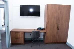 A room with a wooden desk, a grey chair, a television mounted on the wall, and a wardrobe. - Oasis on Beamish Hotel (Campsie)