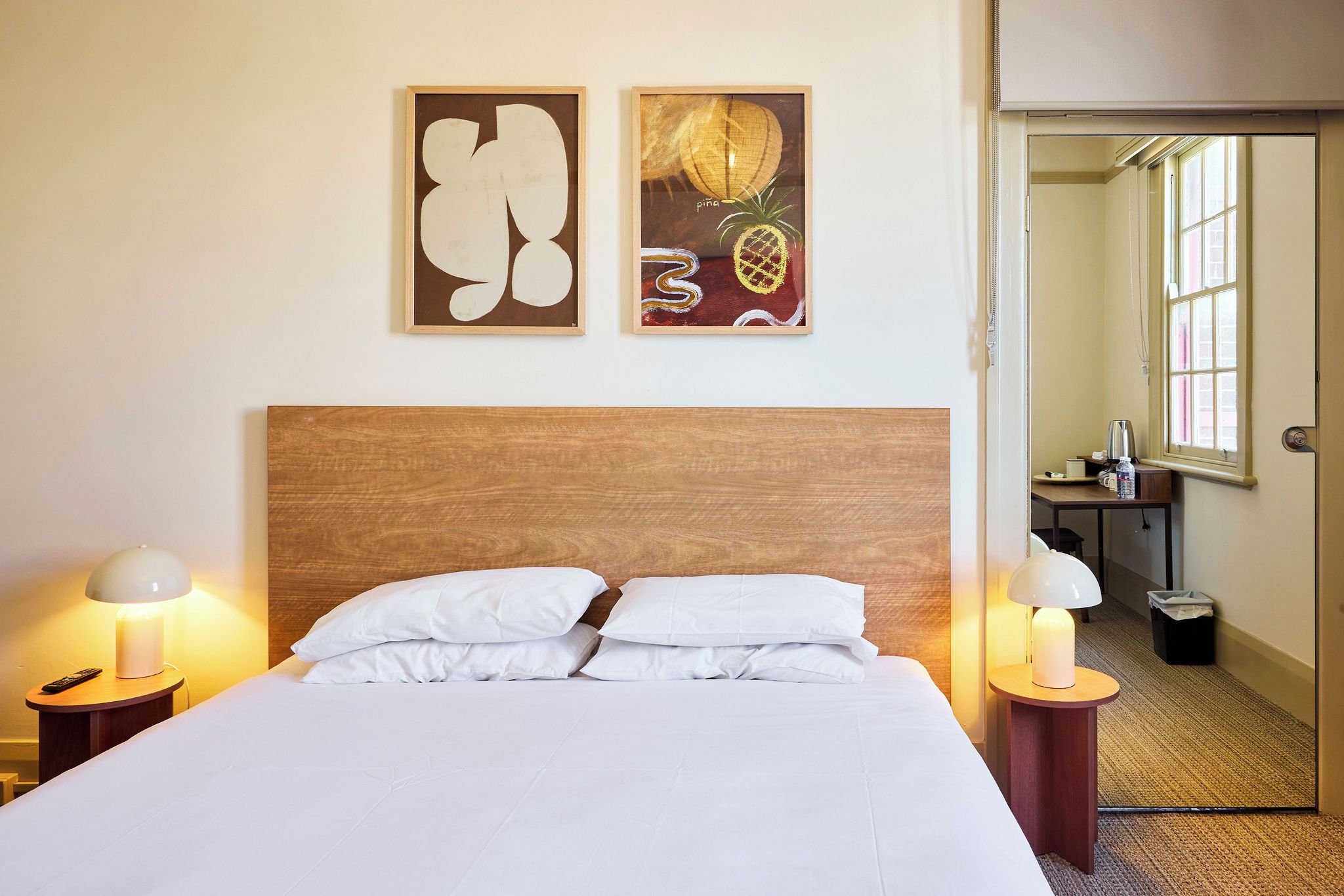 A hotel room with a wooden headboard, white bedding, two bedside lamps, and artwork on the wall.