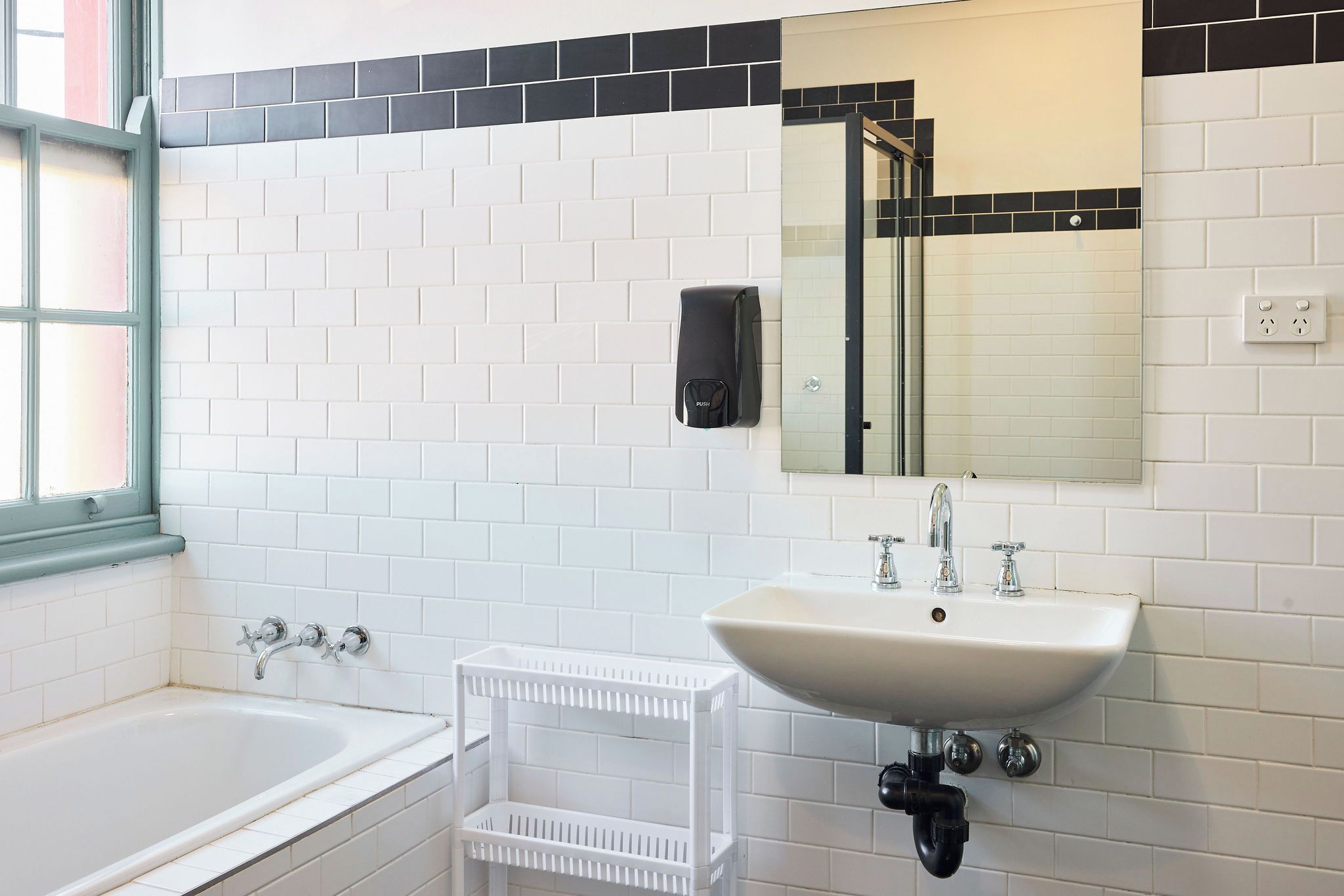 A bathroom with a white sink, two faucets, a mirror, and a window.