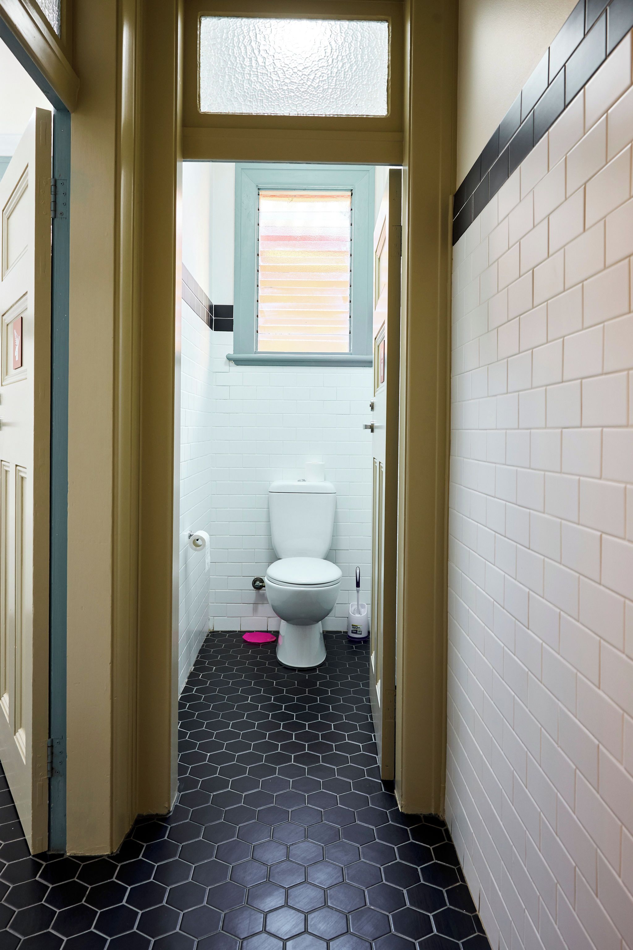 Un pasillo estrecho que conduce a un baño con inodoro, ventana y suelo de baldosas.