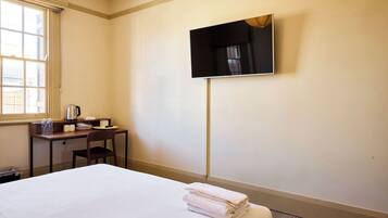 A hotel room with a bed, a desk, a chair, a flat-screen TV mounted on the wall, and a window.