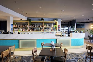 A bar area with a counter, seating, and a variety of bottles. - Oasis on Beamish Hotel (Campsie)