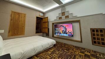 A hotel room with a bed, wooden wardrobe, a television mounted on the wall, and a patterned floor.