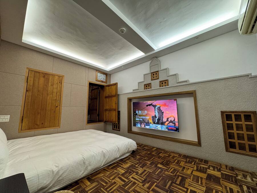 A hotel room with a bed, wooden wardrobe, a television mounted on the wall, and a patterned floor.